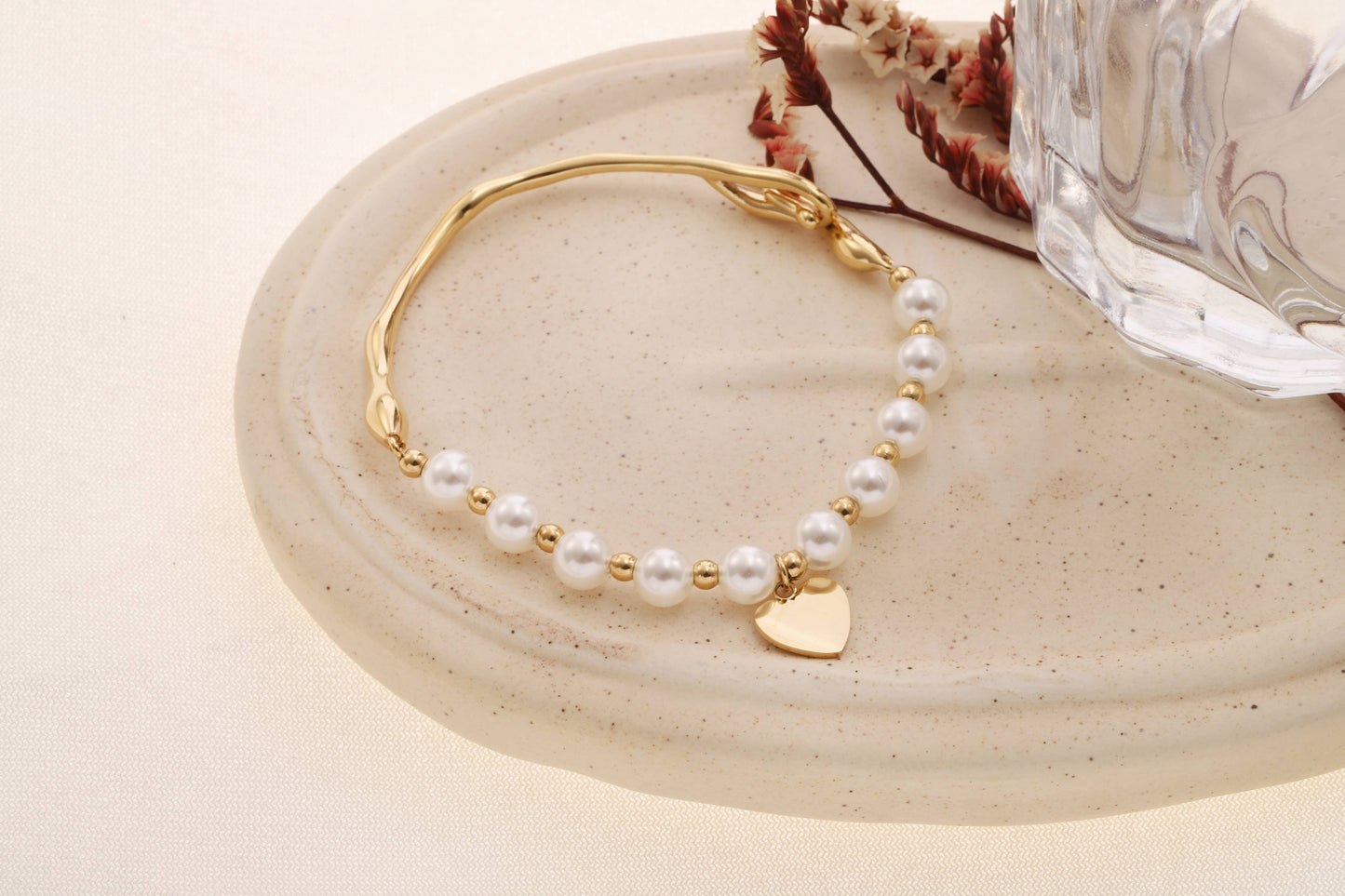 Elegant halvstyvt guldarmband med vita pärlor och hjärthänge